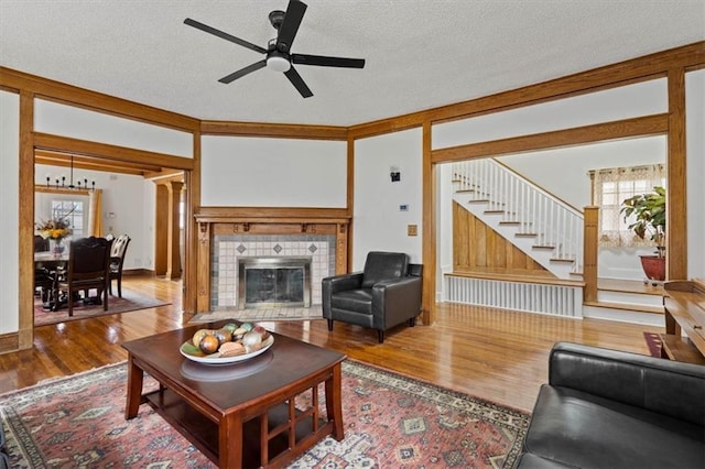 3820 Virginia Ave, Kansas City, MO 64109 - living room featuring ceiling fan, a textured ceiling, a tiled fireplace, wood finished floors, and stairs