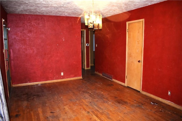 spare room featuring baseboards, visible vents, a textured ceiling, and hardwood / wood-style floors