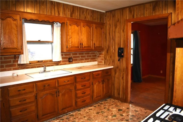 kitchen featuring brown cabinetry, light countertops, a sink, and wood walls