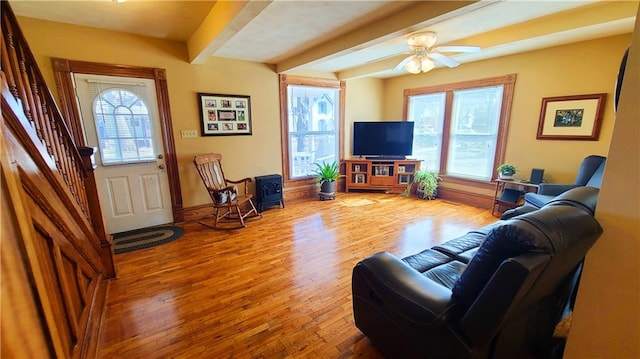 living area featuring beamed ceiling, a ceiling fan, wood finished floors, and stairs