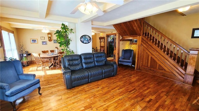 living area featuring beam ceiling, stairway, ceiling fan, and light wood-style floors