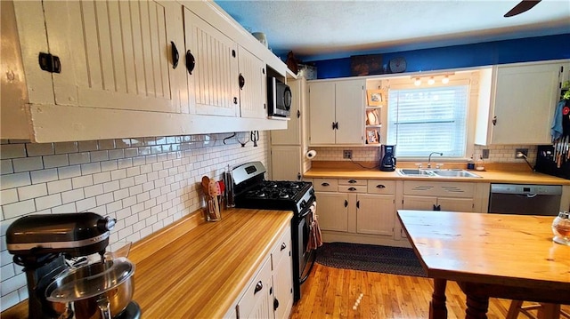 kitchen featuring backsplash, light wood-style flooring, stainless steel appliances, white cabinetry, and a sink