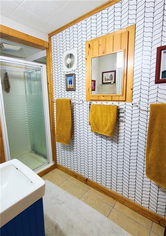 full bath with tile patterned floors, a drop ceiling, a shower stall, and wallpapered walls