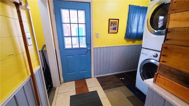 laundry area featuring laundry area, light tile patterned flooring, stacked washer and clothes dryer, and wainscoting