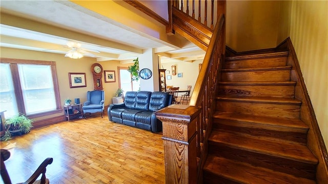 living room featuring beamed ceiling, stairway, light wood-style flooring, and a ceiling fan