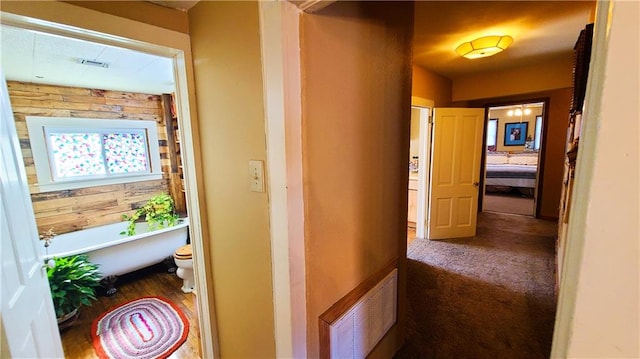 hall featuring visible vents, carpet flooring, and wooden walls