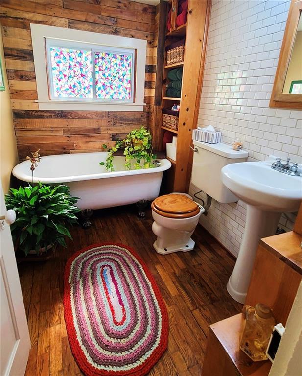 full bathroom featuring toilet, wood finished floors, wood walls, and a freestanding bath