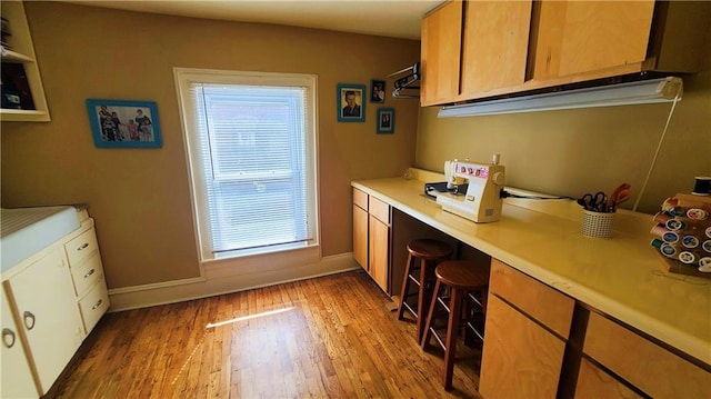 kitchen featuring baseboards, a breakfast bar, light wood-type flooring, light countertops, and built in study area