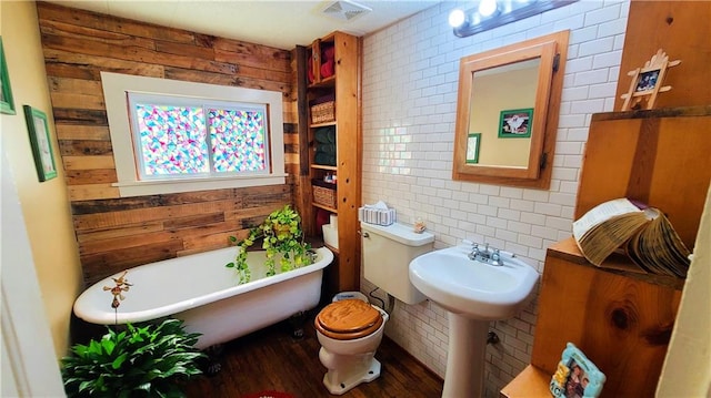 full bath featuring a soaking tub, visible vents, wood walls, and toilet