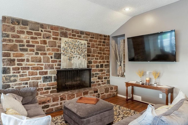 living area with a textured ceiling, lofted ceiling, a large fireplace, wood finished floors, and baseboards