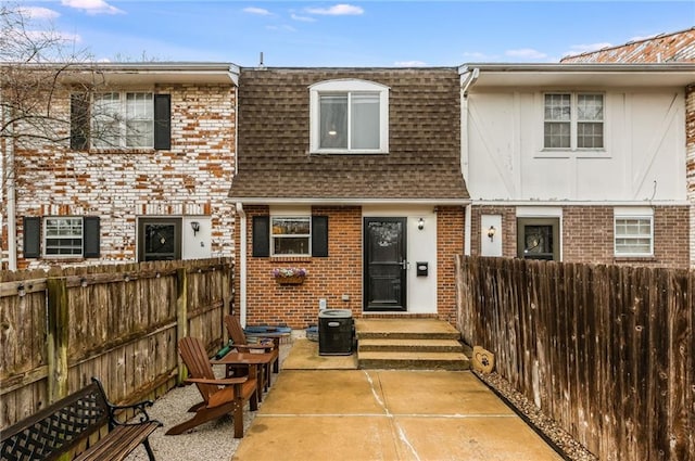 multi unit property featuring a shingled roof, brick siding, fence, and mansard roof