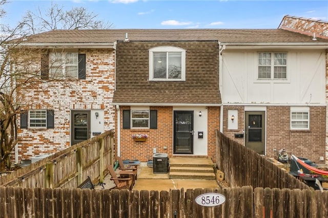 multi unit property featuring a shingled roof, brick siding, a fenced backyard, and mansard roof