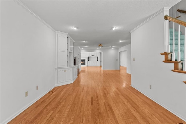 interior space featuring crown molding, ceiling fan, light wood-style flooring, stairs, and baseboards
