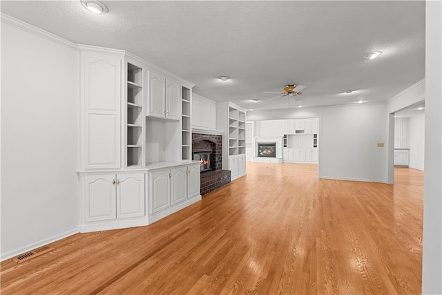 unfurnished living room with a brick fireplace, visible vents, a ceiling fan, and a textured ceiling