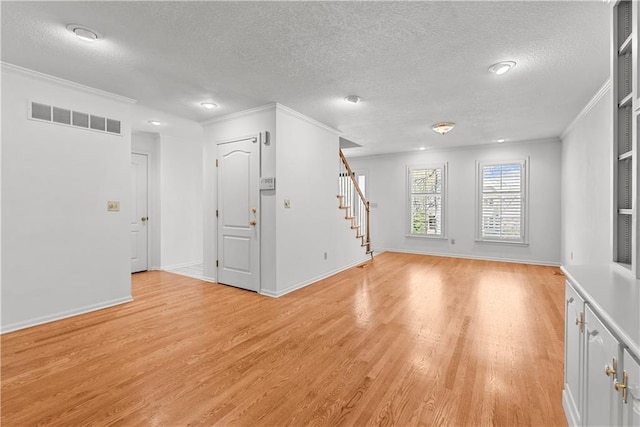unfurnished living room featuring visible vents, light wood-type flooring, a textured ceiling, crown molding, and stairs