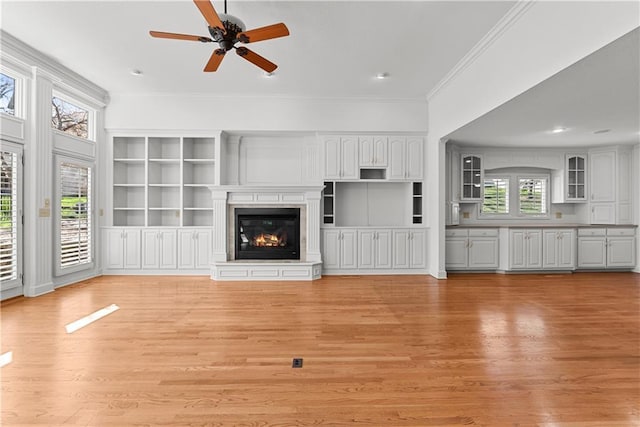 unfurnished living room featuring a glass covered fireplace, ornamental molding, recessed lighting, ceiling fan, and light wood finished floors