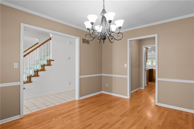 spare room with light wood finished floors, visible vents, an inviting chandelier, and crown molding