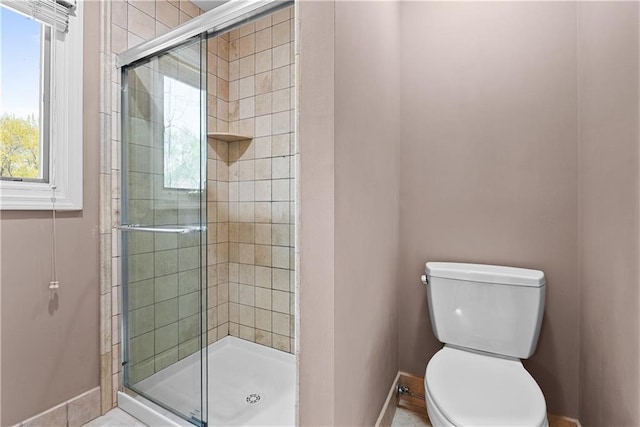 bathroom with toilet, baseboards, and a stall shower