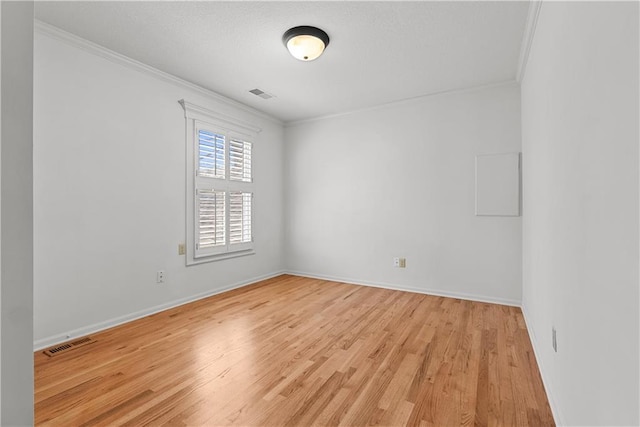 empty room with crown molding, visible vents, light wood-style flooring, and baseboards