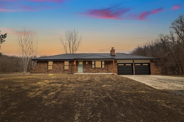 view of front of home with driveway, an attached garage, metal roof, brick siding, and a chimney