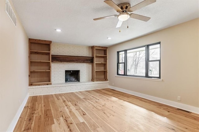 unfurnished living room featuring visible vents, a textured ceiling, baseboards, and wood finished floors