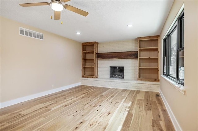 unfurnished living room with visible vents, baseboards, a brick fireplace, and light wood finished floors