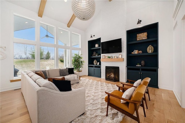 living area with high vaulted ceiling, a brick fireplace, beam ceiling, and light wood-style flooring