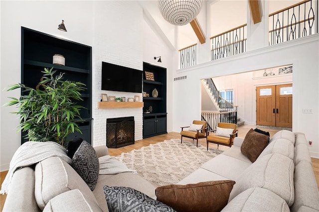 living area with visible vents, wood finished floors, a high ceiling, stairs, and a brick fireplace