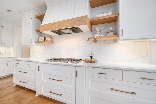 kitchen featuring light wood-style floors, custom range hood, stainless steel gas cooktop, and open shelves