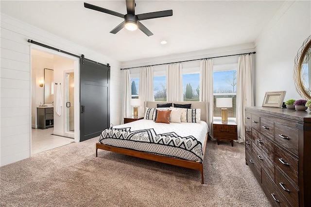 bedroom featuring ceiling fan, a barn door, ensuite bathroom, and light colored carpet