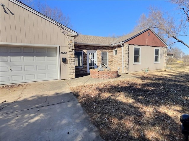 ranch-style house featuring an attached garage, stone siding, a shingled roof, and concrete driveway