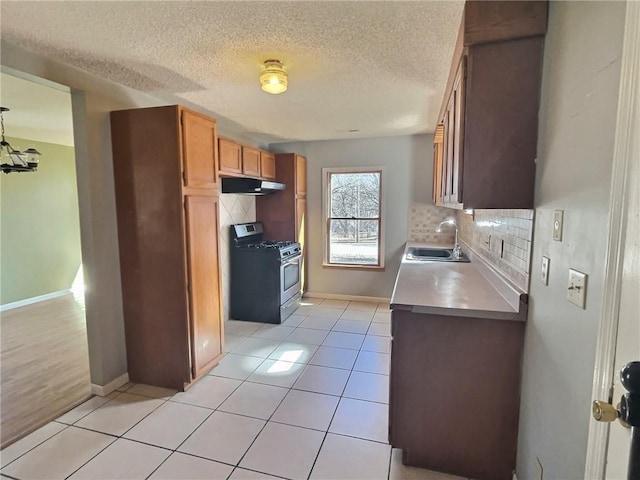 kitchen with light tile patterned floors, gas stove, a sink, and under cabinet range hood