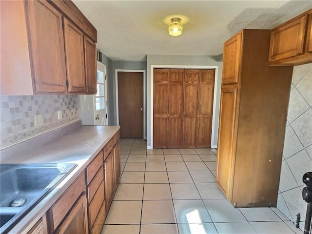 kitchen with light countertops, decorative backsplash, brown cabinetry, light tile patterned flooring, and a sink