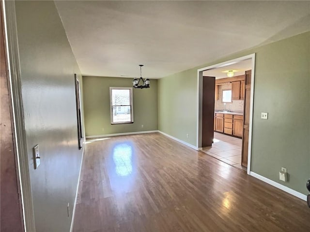 spare room featuring baseboards, light wood finished floors, a sink, and a notable chandelier