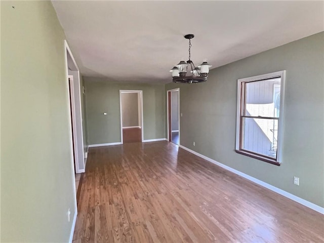 spare room featuring baseboards, wood finished floors, and an inviting chandelier