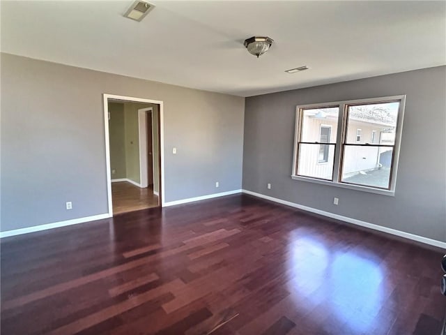 empty room featuring dark wood finished floors, visible vents, and baseboards