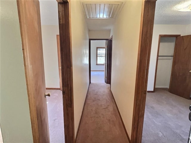 hall featuring a textured ceiling, carpet flooring, and baseboards