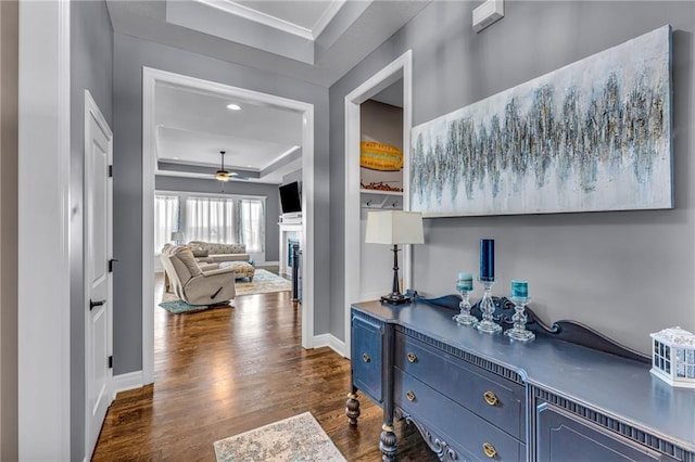 hallway featuring crown molding, a raised ceiling, dark wood finished floors, and baseboards