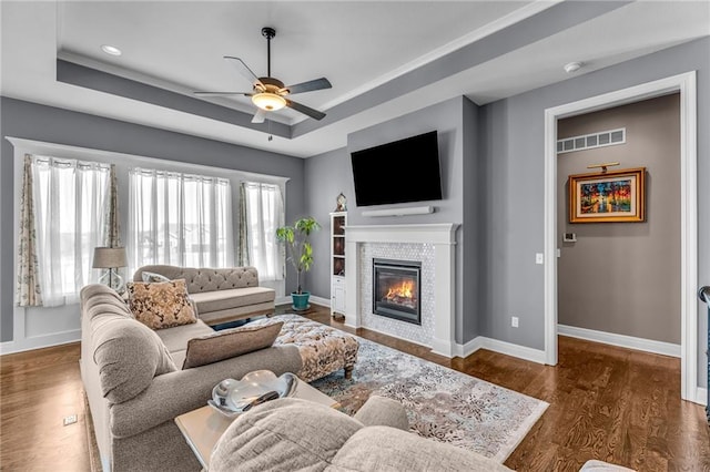 living area with baseboards, visible vents, a raised ceiling, and wood finished floors