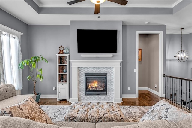 living room featuring a tray ceiling, a fireplace, wood finished floors, and baseboards