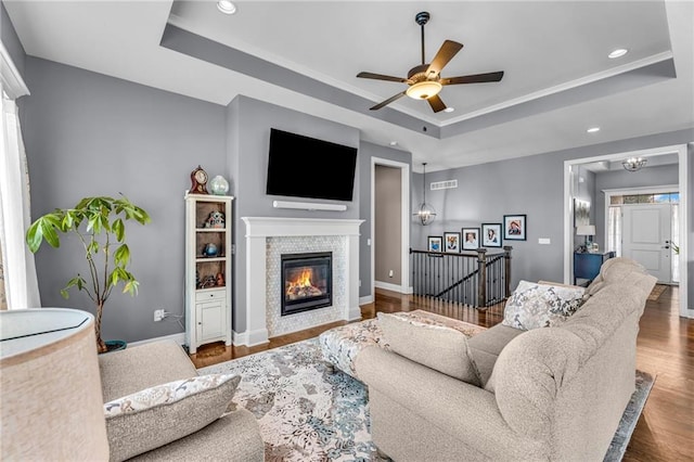 living area with a tray ceiling, recessed lighting, a glass covered fireplace, wood finished floors, and baseboards