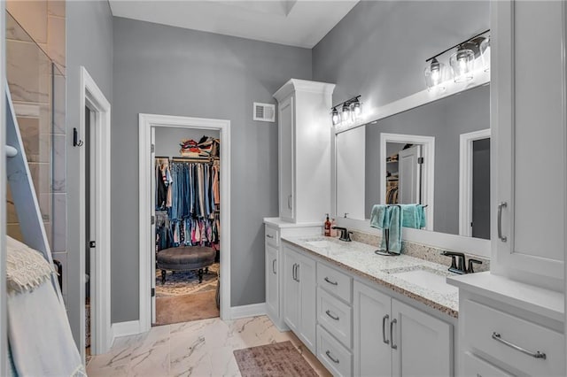 bathroom with a sink, visible vents, marble finish floor, double vanity, and a walk in closet