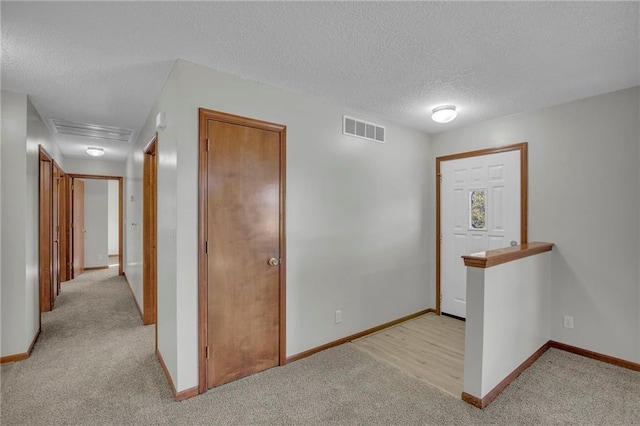 hallway featuring visible vents, light carpet, and baseboards