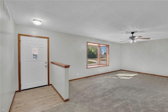 entryway with light carpet, baseboards, visible vents, a ceiling fan, and a textured ceiling