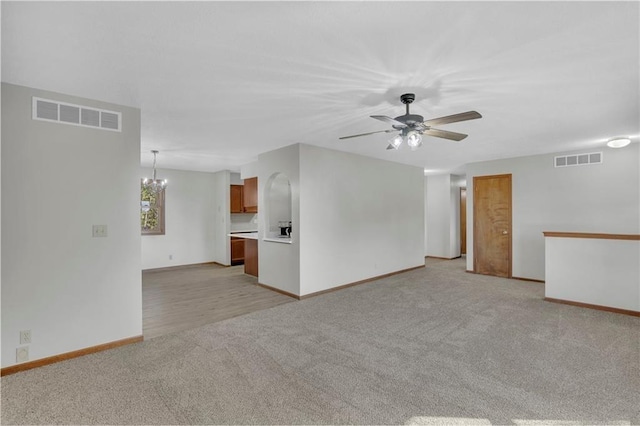 unfurnished living room with ceiling fan with notable chandelier, baseboards, visible vents, and light colored carpet