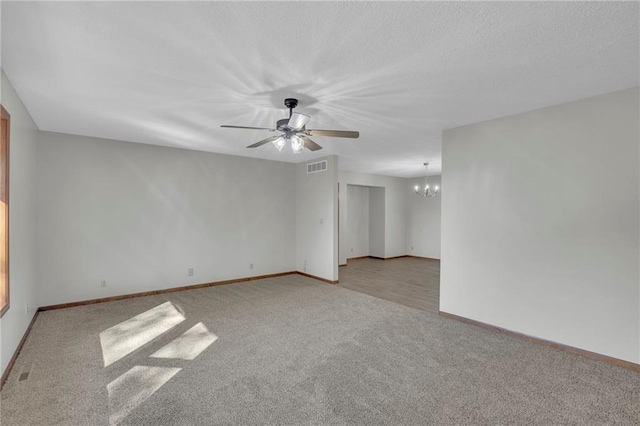 spare room featuring ceiling fan with notable chandelier, carpet, visible vents, and baseboards