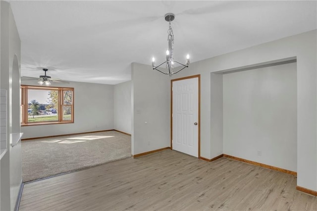 unfurnished room featuring ceiling fan with notable chandelier, wood finished floors, and baseboards