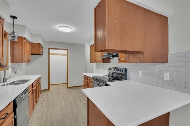 kitchen featuring light countertops, appliances with stainless steel finishes, brown cabinetry, a sink, and under cabinet range hood