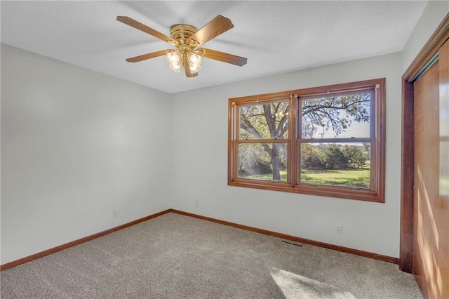 carpeted spare room featuring ceiling fan, visible vents, and baseboards