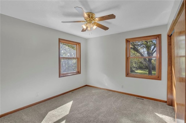 carpeted empty room with baseboards, visible vents, and ceiling fan